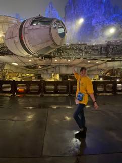 Image of a person in t-shirt and pants standing in front of a spaceship from the Star Wars movies after dark